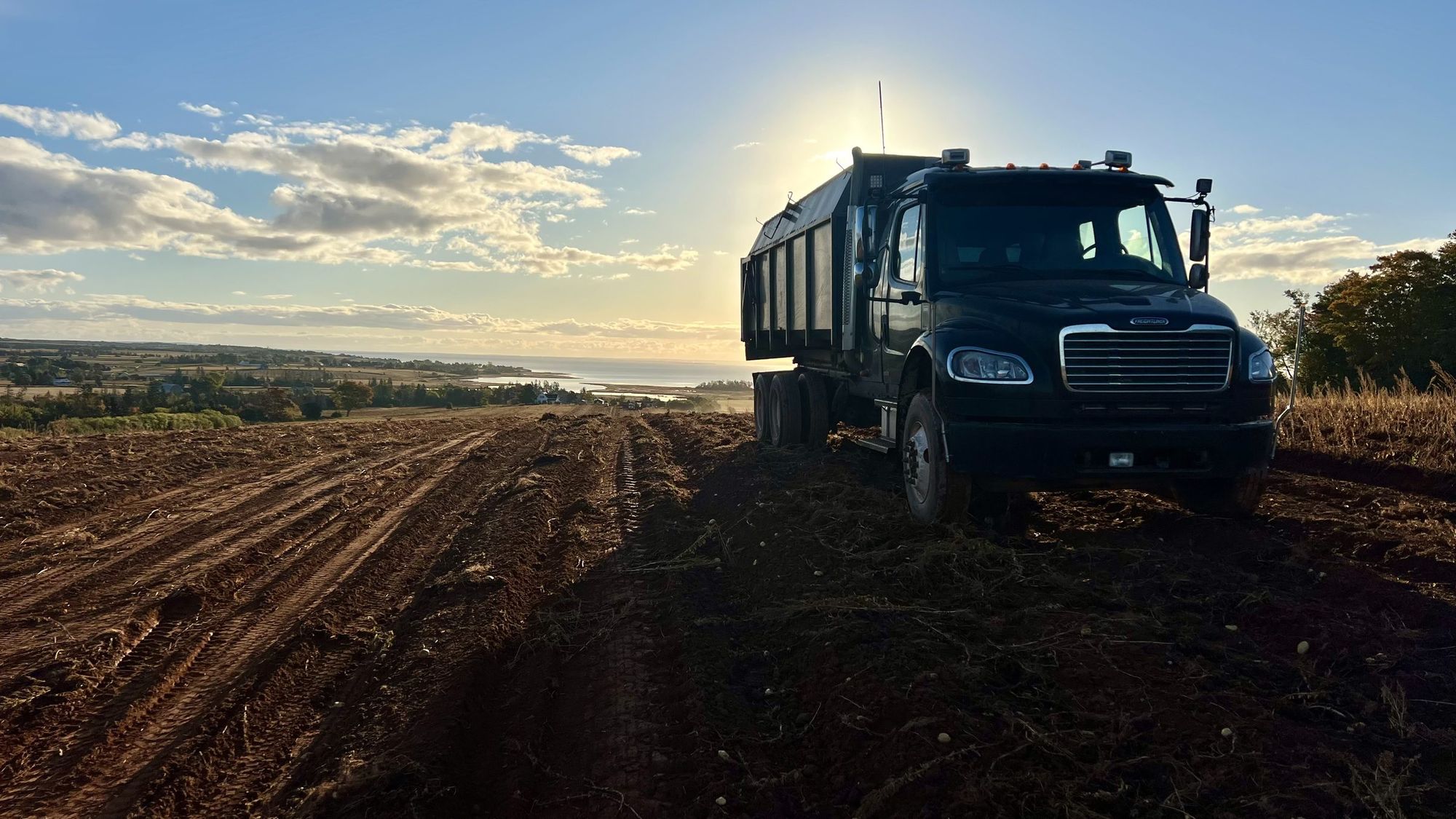 A farm truck on a red-soil field at dusk on Prince Edward Island